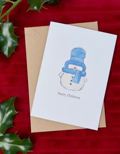 a christmas card with a snowman wearing a blue hat and scarf on top of it