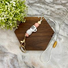 a wooden keychain with a white and pink bead on it sitting next to a potted plant