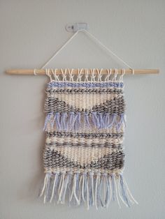 a woven wall hanging on a white wall next to a wooden hanger filled with yarn