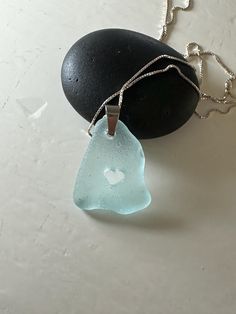 two pieces of sea glass sitting on top of a rock next to a chain necklace