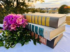 three books stacked on top of each other next to a bouquet of purple and green flowers