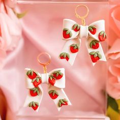 two bows with strawberries on them are hanging from earwires in front of pink flowers