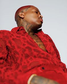 a man in a red shirt with tattoos on his arm and chest, sitting down