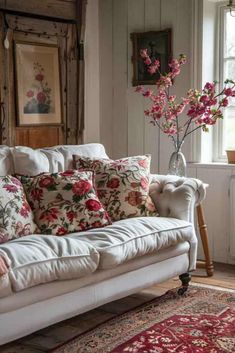 a white couch sitting in front of a window filled with pink flowers on top of a rug