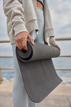 a person holding a yoga mat near the ocean