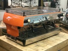 an orange espresso machine sitting on top of a wooden table