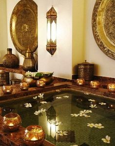 an indoor hot tub with candles and flowers on the water in front of two wall hangings