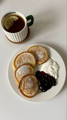 some powdered sugar and jelly are on a plate next to a cup of coffee