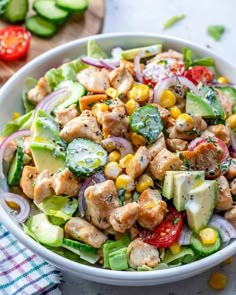 a white bowl filled with chicken, cucumber and tomato salad on top of a table