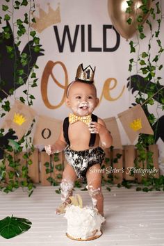 a baby wearing a crown standing on top of a cake in front of a backdrop