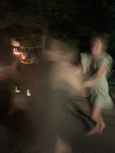 blurry image of two people dancing in the street at night, with lights on