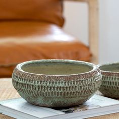 two green bowls sitting on top of a table next to a brown leather chair and ottoman