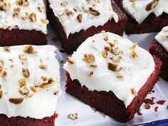 several pieces of red velvet cake with white frosting and walnuts on top, sitting on a plate