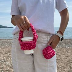 a person holding a coffee cup in their hand and some pink crocheted items