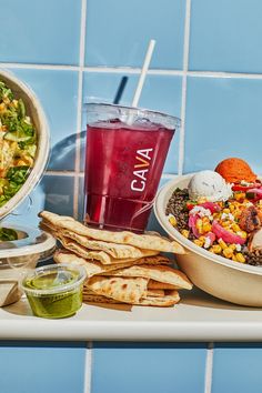 a table topped with bowls of food next to a bowl of salad and a drink