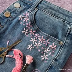 some scissors and thread are laying on the back of a pair of jeans with pink flowers