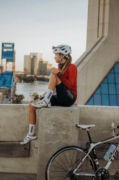 a woman sitting on top of a cement wall next to a bike