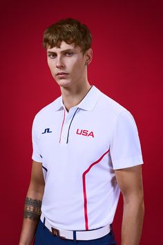 a man in a white polo shirt and blue pants poses for a photo against a red background