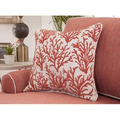 a red and white pillow sitting on top of a couch next to a plant in a vase