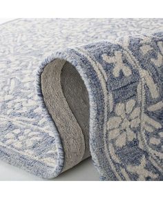 a blue and white rug laying on top of a white floor next to a wall