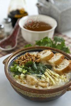 a bowl of soup on a table with bread and greens next to a cup of tea