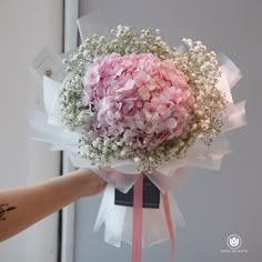 a bouquet of pink and white flowers is being held by a woman's hand