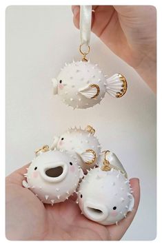 three white ceramic ornaments in the shape of fish and sea urchins are being held by someone's hand