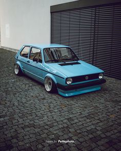 a blue car parked in front of a garage door on a cobblestone street