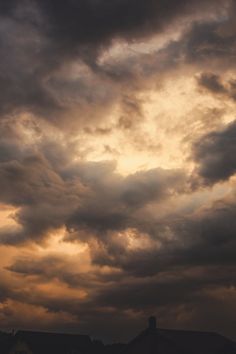 the sky is filled with dark clouds and some houses in the distance are silhouetted