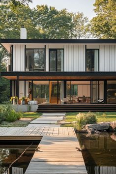 a modern house with a dock leading to the front door and covered patio area that is surrounded by trees