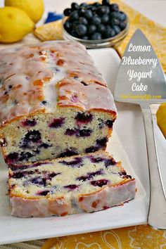 a loaf of lemon blueberry yogurt cake on a white plate next to some fruit