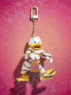 a ducky keychain with a bag hanging from it's side on a pink surface