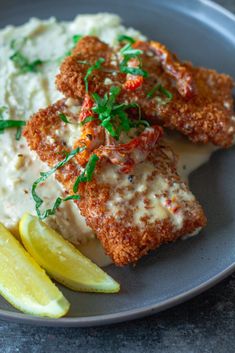 two pieces of fried fish with mashed potatoes and lemon wedges