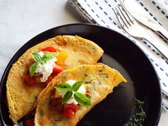 two tortillas on a black plate topped with cheese and vegtables