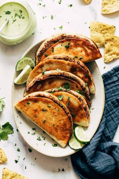 a white plate topped with quesadillas next to chips and lime wedges