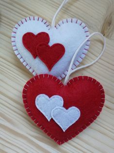 two red and white heart shaped ornaments hanging from strings on a wooden table with string