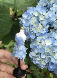 a person is holding a small figurine in front of some blue hydrangeas