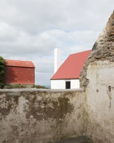 an old stone wall with a red roof next to a white building on the other side