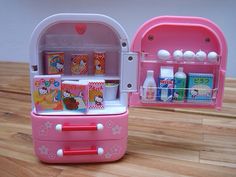 a pink toy refrigerator sitting on top of a wooden table next to a plastic cup holder