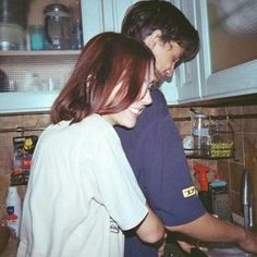 two people are standing in the kitchen preparing food and smiling at each other's faces