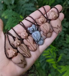 a hand holding five small clay animals on brown string with green plants in the background