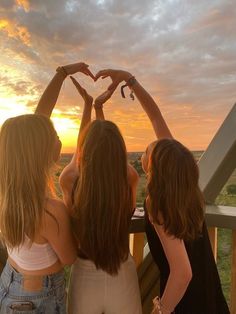 three girls standing on a balcony making a heart shape with their hands at the sunset