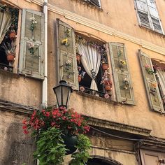 an old building with shutters open and flowers hanging from it's window sill