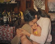 a woman holding a small child in her arms while sitting on the floor next to a table