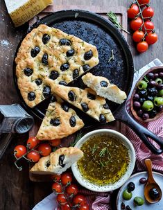 an assortment of olives, tomatoes and bread on a table with other food items