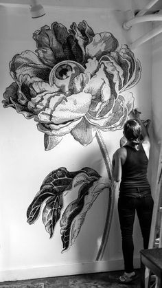 a woman standing in front of a wall with flowers painted on the side and behind her is a black and white photo