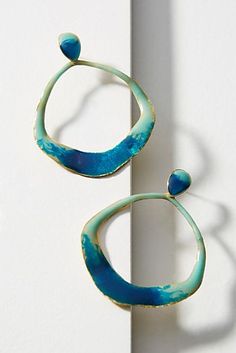 a pair of blue and green earrings sitting on top of a white wall