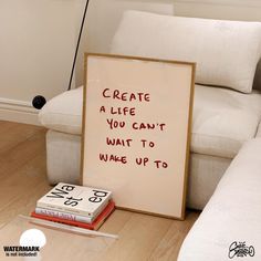 a sign sitting on top of a wooden floor next to a pile of books and a white couch