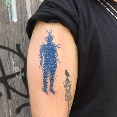 a man's arm with a blue ink drawing of a person and a bird on it