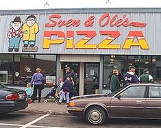 cars parked in front of a pizza shop with people walking around the building and on the sidewalk